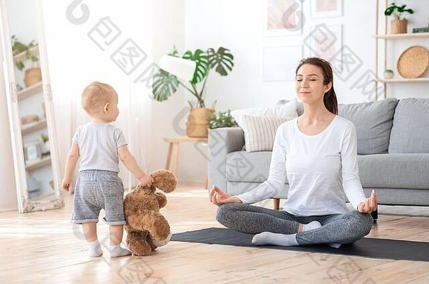 年轻的妈妈在家练习瑜伽，坐在宝宝旁边冥想