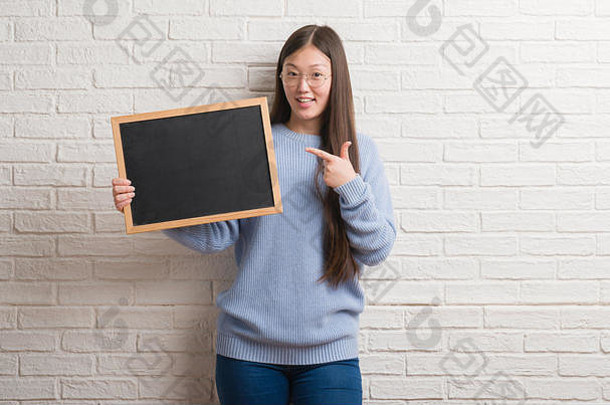 年轻的中国人女人砖墙持有黑板上快乐指出手手指