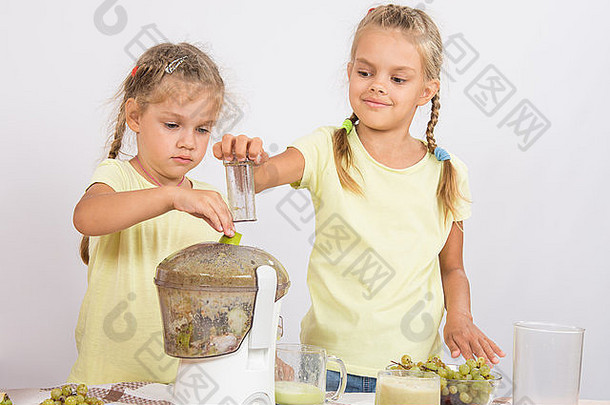 桌上的两个女孩用榨汁机从梨和葡萄中榨汁
