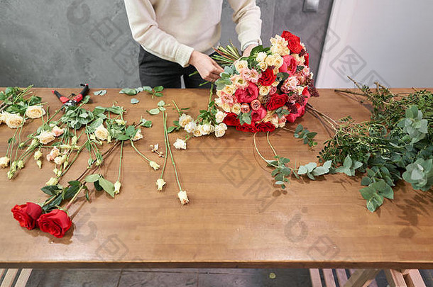 欧洲花店概念。花店女人创造了一束美丽的红色混合花。漂亮的新鲜的一束。教育、硕士班和