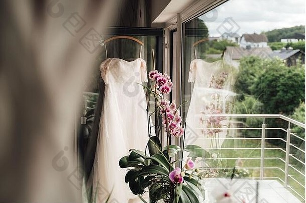 白色婚礼衣服悬挂器挂阳台通过semi-reflected衣服大窗口色彩斑斓的盛开的兰<strong>花花</strong>
