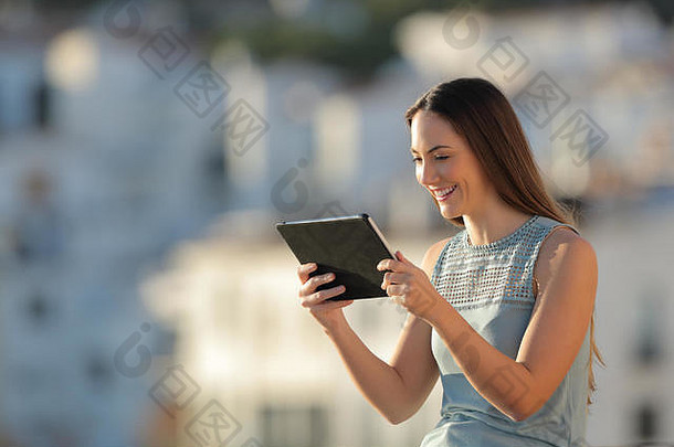 日落时分，快乐女人正在一个小镇的平板电脑上观看媒体内容