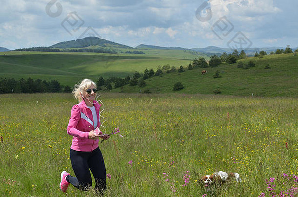 这名妇女带着她的狗，戴着耳机在塞尔维亚兹拉提博尔山的小山上跑步