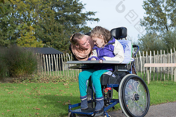 一个坐在轮椅上的残疾儿童，由一名志愿护理人员照料