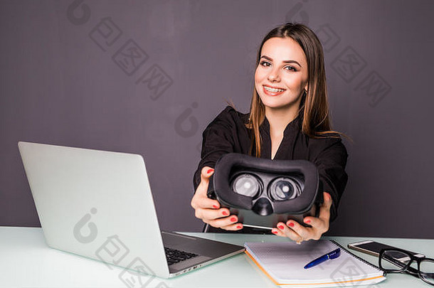 虚拟现实技术。坐在办公室工作地点时，戴着虚拟现实耳机的自信的年轻女子指着天空