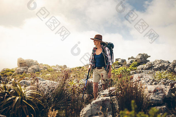 一个手持<strong>登山杖</strong>在岩石山上行走的女人。在徒步探险中戴着帽子和背包的女人。