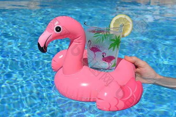 一名妇女拿着一个粉红色的火烈鸟充气饮料杯，杯上装饰着手掌、火烈鸟和一片柠檬。欢乐夏日氛围