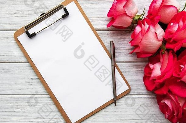 首页办公室桌子上工作空间空白纸剪贴板红色的玫瑰花束白色背景平铺