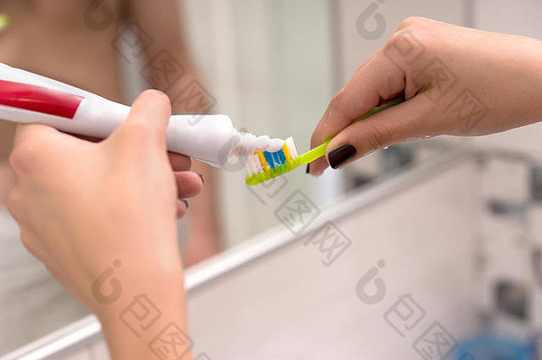 在现代化的瓷砖浴室里，双手拿着牙刷，在镜子前放上牙膏