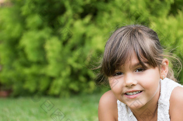 躺在草地上看着相机的微笑美丽小女孩的特写照片。