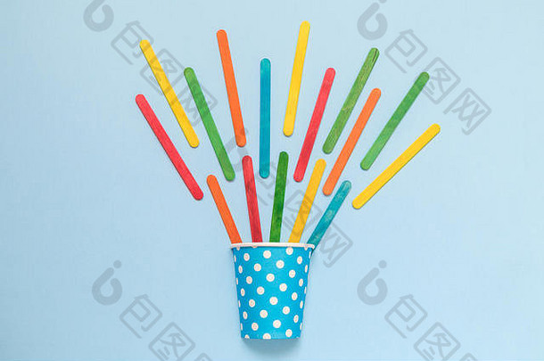 平铺的<strong>纸杯</strong>波尔卡设计和彩色冰淇淋棒在柔和的蓝色背景上，创意概念最少。