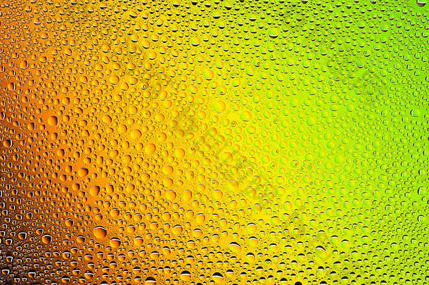 在黄色、橙色、绿色和棕色渐变背景上拍摄水滴的特写镜头，上面覆盖着水滴凝结物。