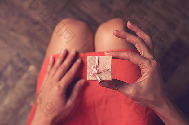 身着粉色连衣裙的女士在膝盖上方打开一个小礼盒的俯视图
