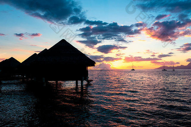 在塔希提岛，茅草屋顶上的夕阳和<strong>帆船</strong>在水上的小屋