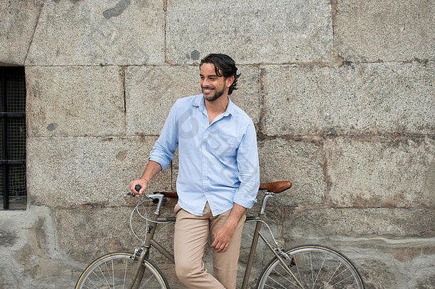 年轻快乐迷人的拉丁男子，穿着休闲时尚的服装，面带微笑，兴高采烈地骑着复古的酷炫复古自行车，以现代时尚的城市风格生活