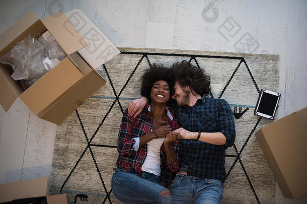 俯视图：一对迷人的多民族年轻夫妇，手牵着手，看着相机，微笑着躺在纸板箱中