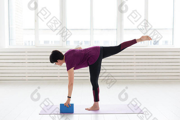 人、瑜伽、运动和保健概念-中年妇女练习瑜伽，使用伸展立方体