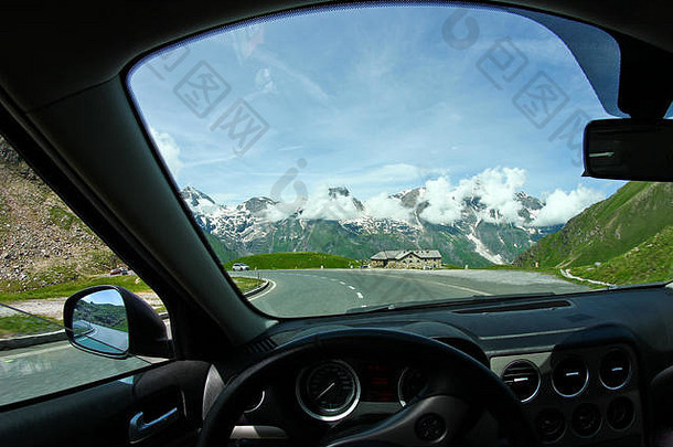 在弯道上行驶时，透过汽车挡风玻璃看到阿尔卑斯山的景色。