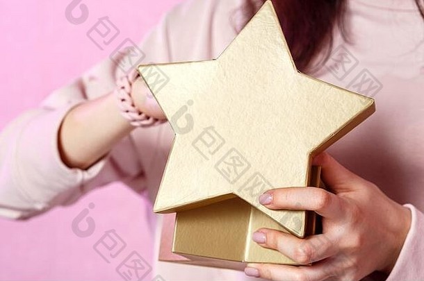 一个年轻的亚洲女孩手中的金星形状的礼品盒。在一个粉红色的孤立背景上