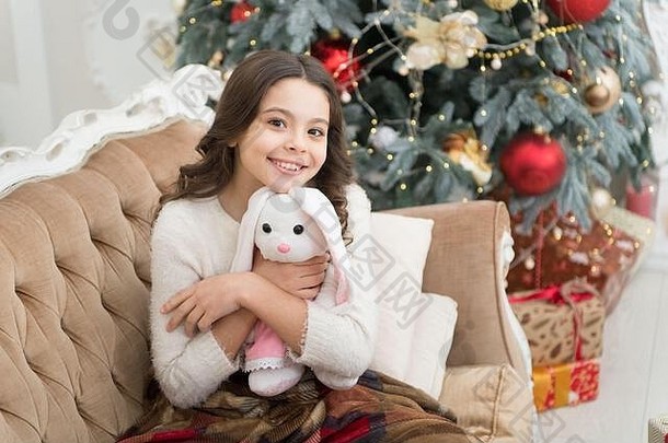 节日快乐。新年快乐。幸福和快乐。准备圣诞礼物。小女孩喜欢她的兔子。最好的圣诞玩具。快乐的孩子在圣诞树旁玩玩具。在家里感觉舒适。