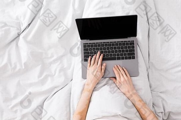 妇女在床上工作，在带有空白屏幕的笔记本电脑上打字