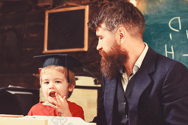 在家教育概念热情的孩子研究老师父亲检查家庭作业帮助男孩儿子老师正式的穿学生学位帽教室黑板背景