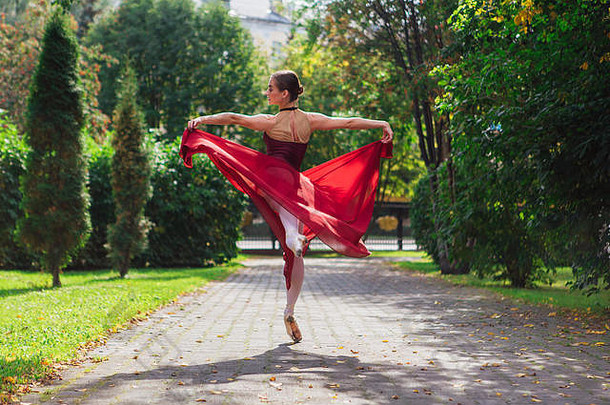 在秋季公园，一位身着红色芭蕾舞服、穿着尖头鞋跳舞的女芭蕾舞演员。