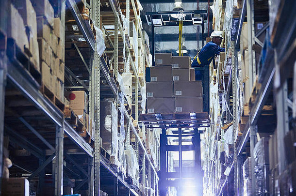操作叉车将纸板箱堆放在配送仓库货架上的工人