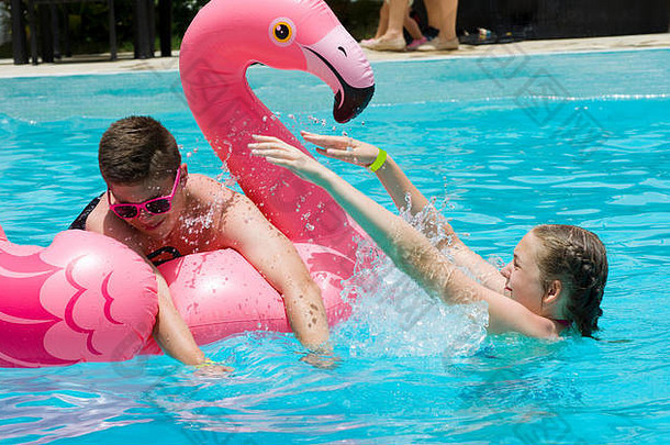 十几岁的女孩男孩玩充气粉红色的火烈鸟奢侈品酒店游泳池夏天假期概念