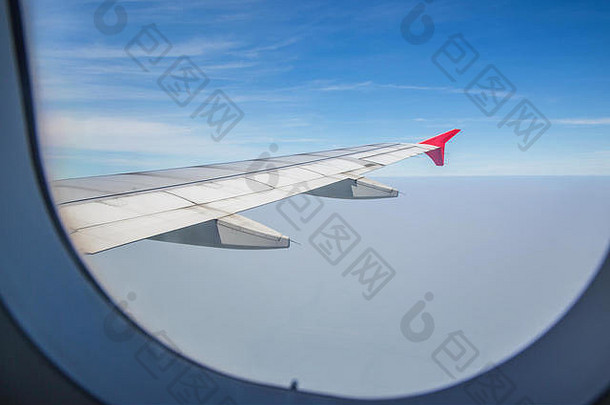 透过一扇窗户看到一架机翼飞机在蓝天的云层上飞行。