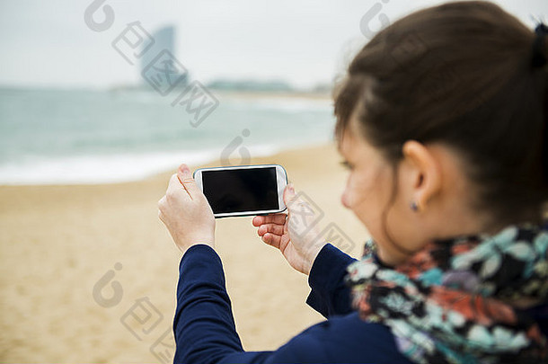 肖像漂亮的年轻的旅行者采取图片细胞电话海滩冷一天