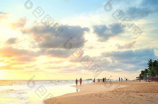 日落时在斯里兰卡海滩上行走的人们