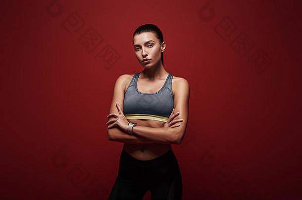 一位身体健康的年轻女运动员交叉双臂站在红色背景上的肖像。