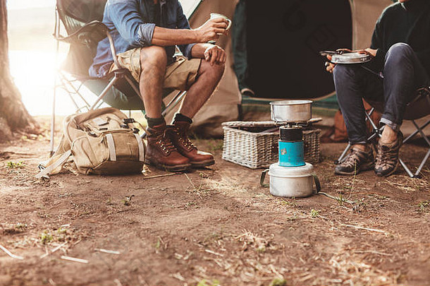 一对夫妇坐在帐篷外，在营地的炉子上煮咖啡的剪影。