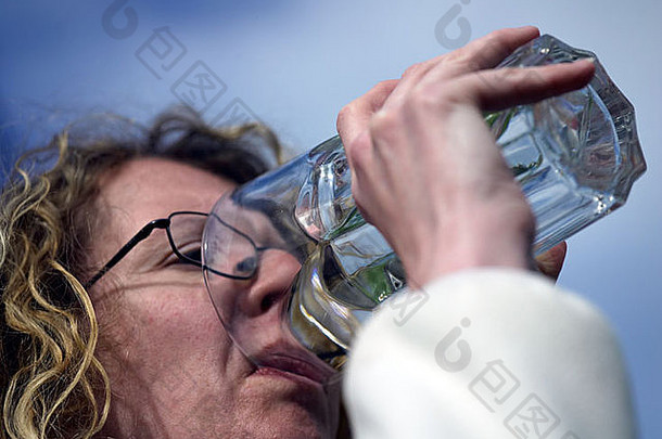阳光明媚的日子里，一位年轻女子在外面喝着一杯咖啡馆风格的大烧杯里的水