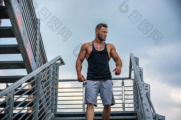 一个肌肉发达的英俊男子站在<strong>城市</strong>的背景下，向一边望去，走下金属楼梯