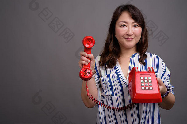 成熟的美丽的亚洲女商人持有红色的电话