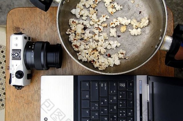 笔记本电脑、数码无镜相机和装有剩余爆米花的罐子的照片。