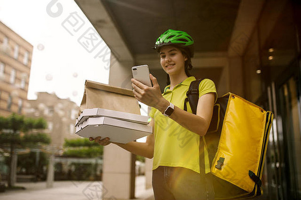 一位身穿黄色衬衫的年轻女子正在运送披萨，她用一些小玩意儿跟踪城市街道上的秩序。使用在线应用程序接收和跟踪发货地址的快递员。现代技术。