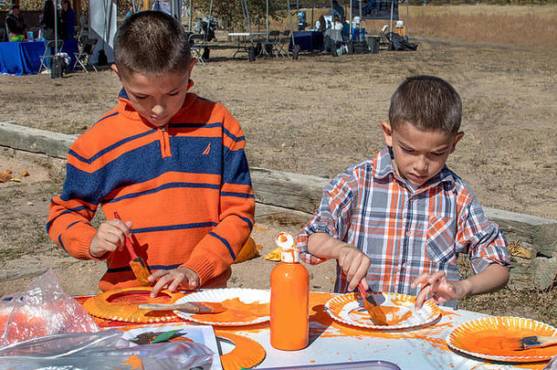 两兄弟在纸盘子上涂上橙色颜料，做一个万圣节装饰<strong>带回家</strong>