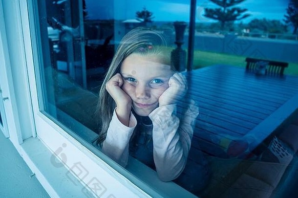 2019冠状病毒疾病隔离期间，沮丧而孤独的小女孩透过窗户看。当科罗纳病毒流行时，孩子们感到悲伤