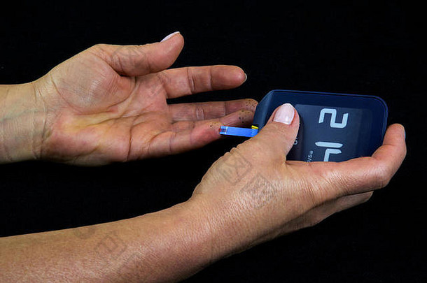一位患有晚期<strong>糖尿病的</strong>妇女使用血糖仪测量血糖水平。一滴血在一条长条上清晰可见