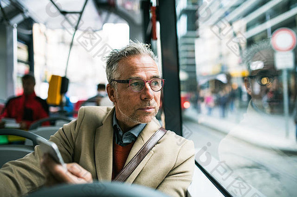 拥有智能手机的成熟商人在城市乘坐公交车出行。