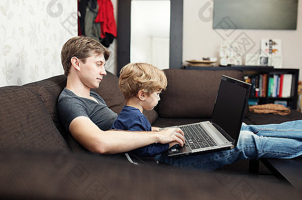 父亲和儿子在家里的沙发上<strong>使用</strong>笔记本电脑