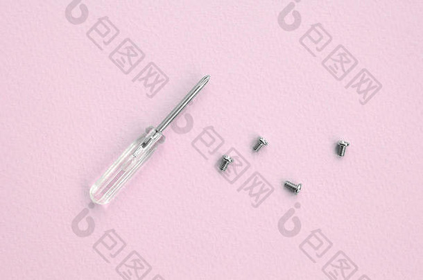 一把小螺丝刀和一些粉红色背景的螺丝。用于维修和拆卸现代智能手机和移动设备的工具