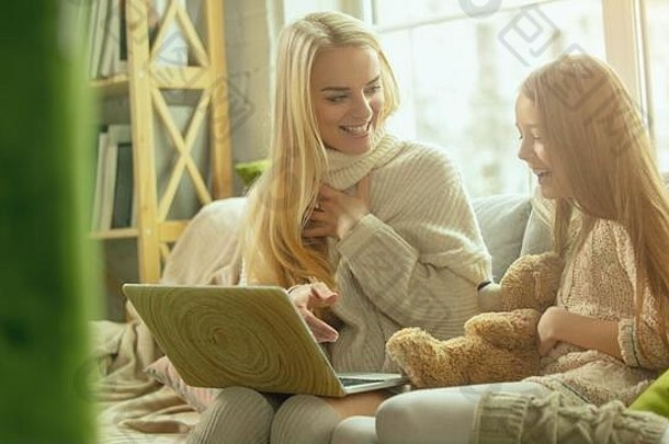玩得开心。幸福的家庭。母亲和女儿一起在家度过时光。看电影，使用笔记本电脑，大笑。母亲节，庆祝活动，周末，节日，童年的概念。