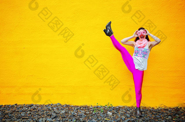 年轻的女人持有甜甜圈脸跳舞前面黄色的墙