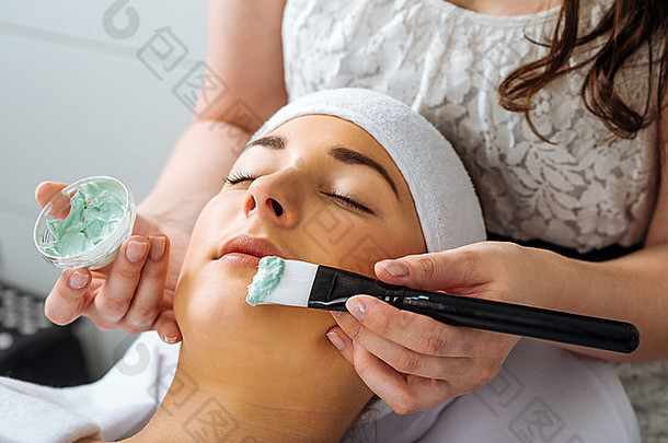 照片中一位年轻漂亮的女孩在SPA美容院接受绿色面膜。