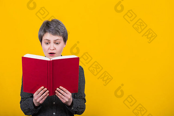 一位表情激动、目瞪口呆的年轻女子在一本书中惊奇地发现了一条令人震惊的文字。惊讶的女学生拿着一本红色的课本，隔着黄色