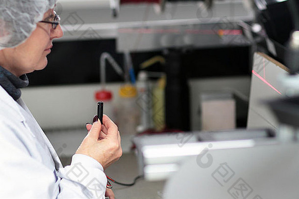 一位身穿洁净室外套的妇女正在一家实验室里为技术设备检查激光